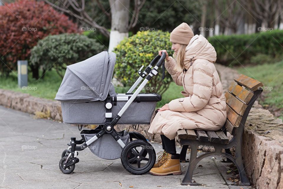 Young Caucasian mother walking outdoor with newborn baby in pram