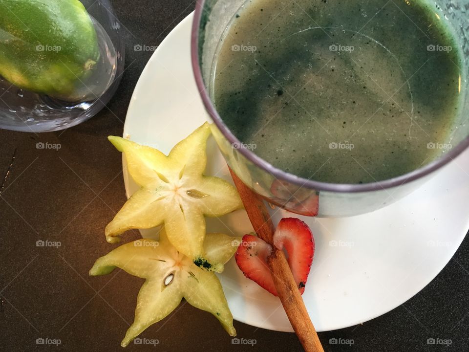 Drinking a fresh fruit and spiroulina green protein rich smoothie on white plate with strawberry heart and cinnamon stir stick 