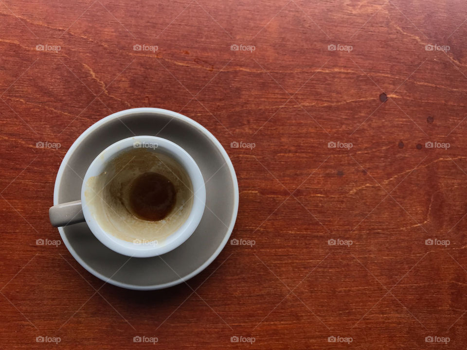 light gray cup and saucer of finished espresso coffee with stained brown coffee in a cup on brown wooden table with copy space on right side of frame