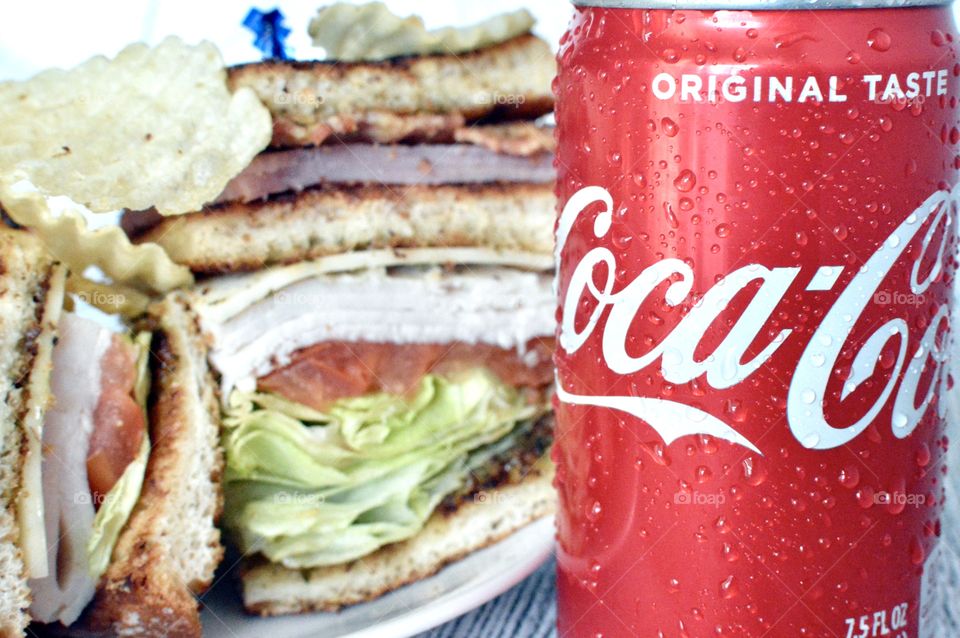 A can of Coca Cola with a club sandwich in the background 