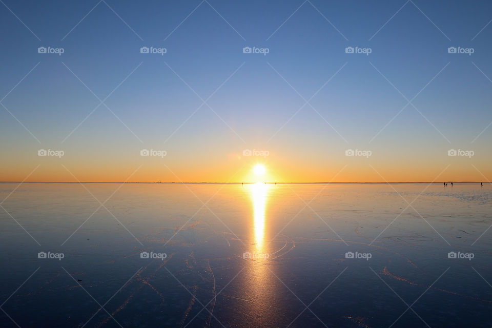 Sunset on ice. Distant people silhouettes skating on the Frozen Öresund strait between Sweden and Denmark, February 2021