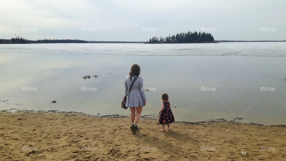 Mother and daughter throwing pebbles into the thawing astotin lake in elk island park, Alberta, Canada 