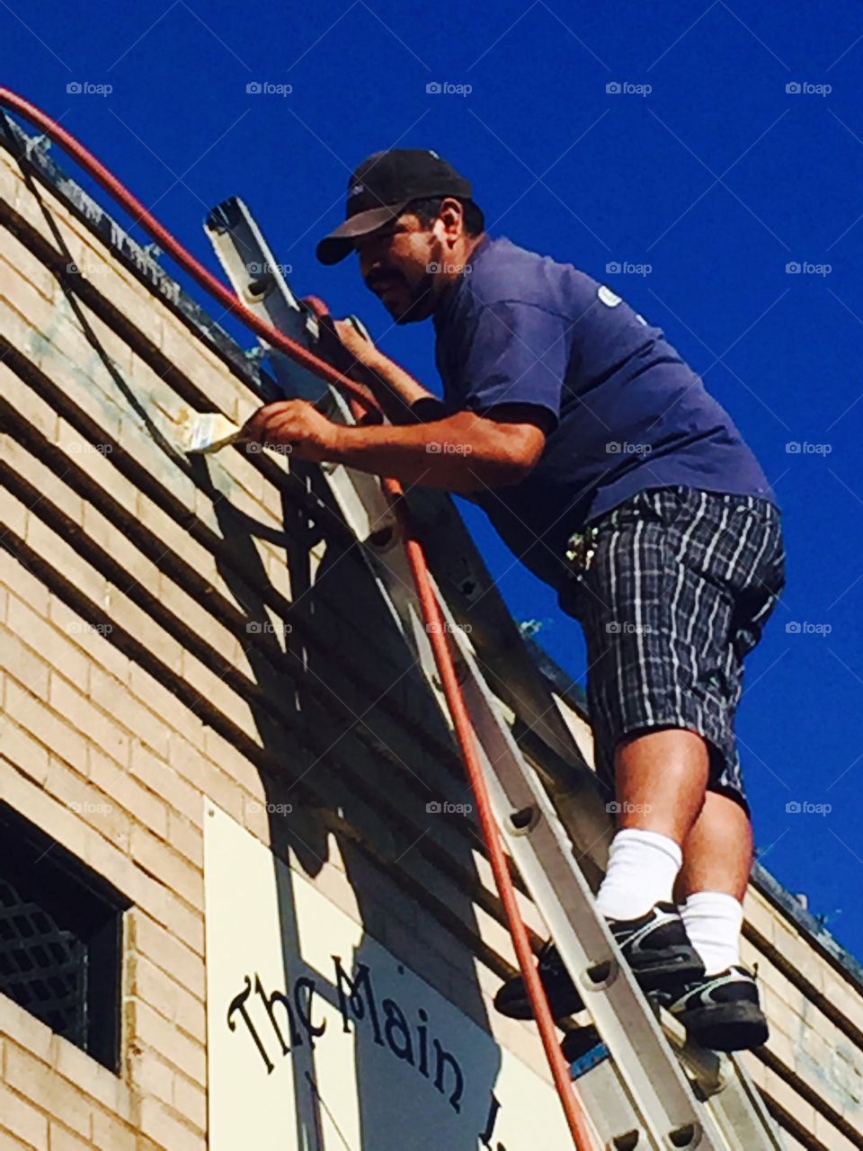Painter on a ladder painting a small business outside 