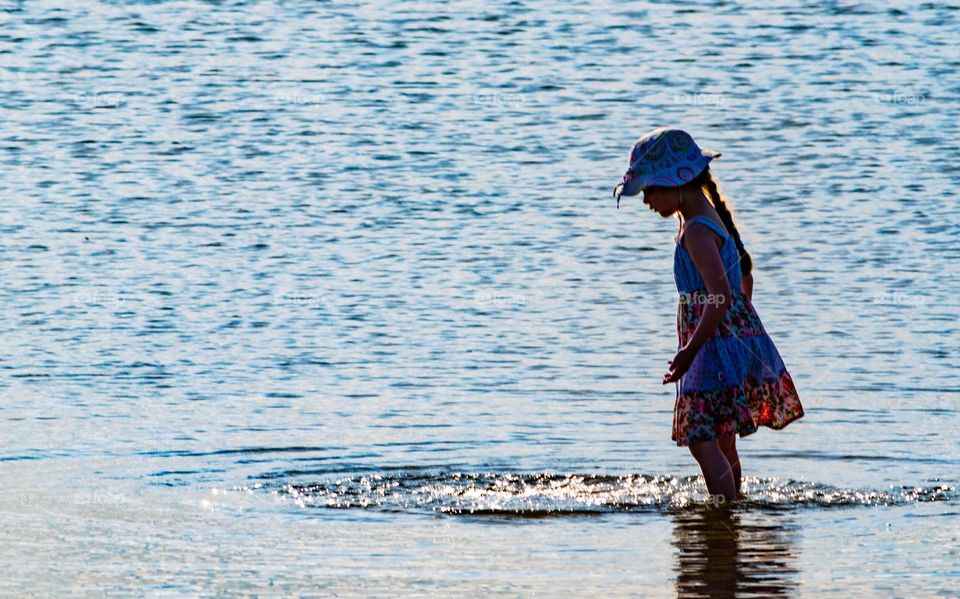 Young girl standing in sea looking at ripples in the water