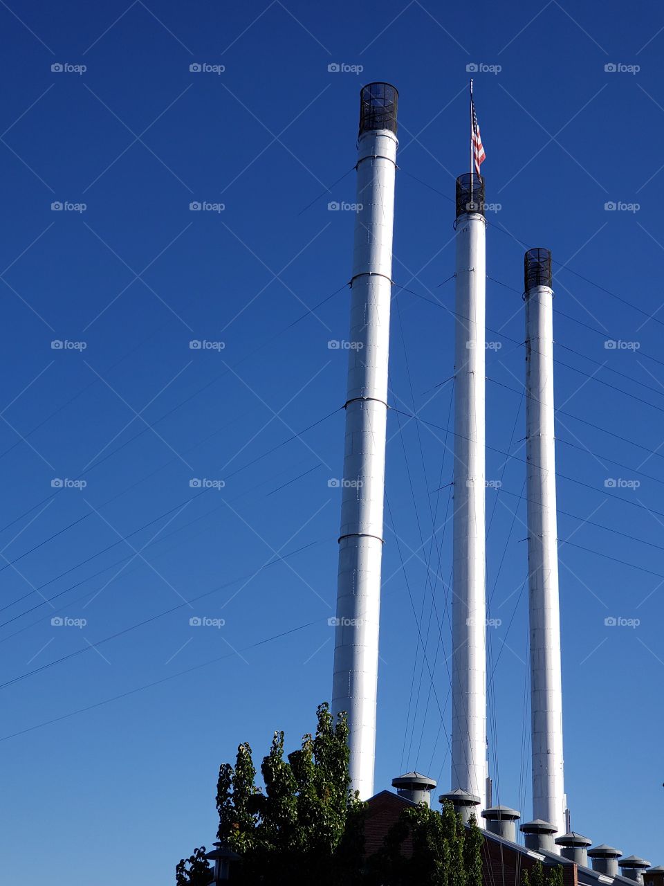 Old smoke stacks from an Oregon Mill no longer in use with an American flag mounted at the top against clear blue skies on a fall morning. 