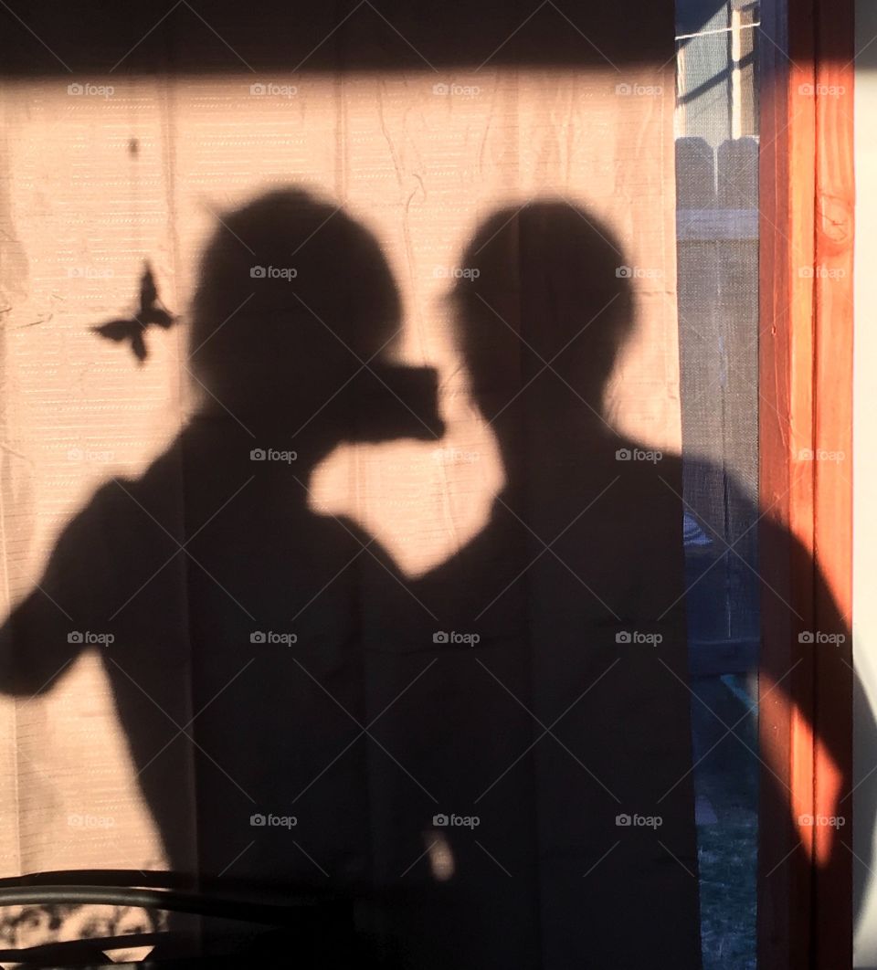 Shadow on wall of two women with mobile phone photographing butterfly 