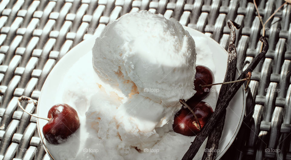 Vanilla ice cream scoops on plate with fresh summer black cherry garnish decorated with vanilla bean pods in sunlight outdoors 