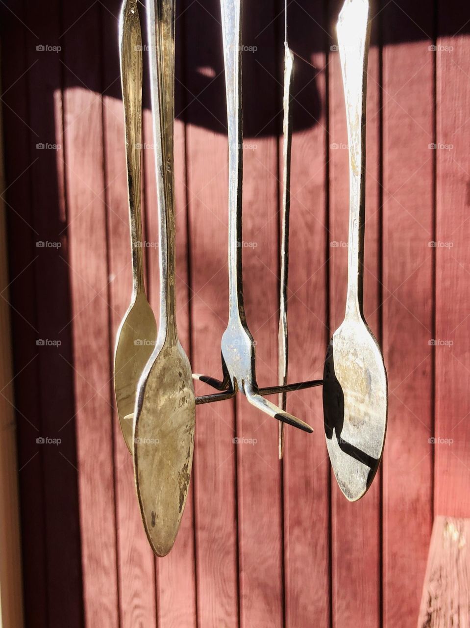 Wind chime of repurposed silverware, with fork in the center clinking against spoons in the sunlight 