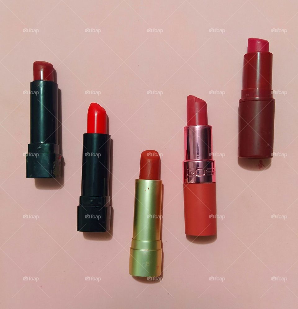 Five shades of red coloured lipsticks against a pink background background captured from above.