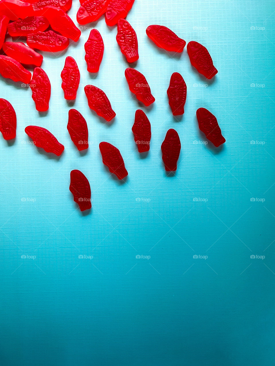 A school of bright red gummy fish in multi toned blue water. 