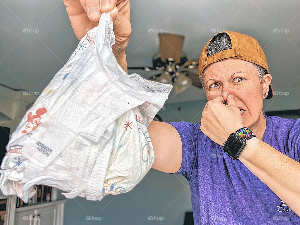 Woman is disgusted by dirty diaper, diaper duty is gross, disgust as an emotion, dirty diaper is disgusting, woman shows emotion of disgust on face, woman is disgusted with dirty diaper and holds nose, woman holds nose for stinky diaper 