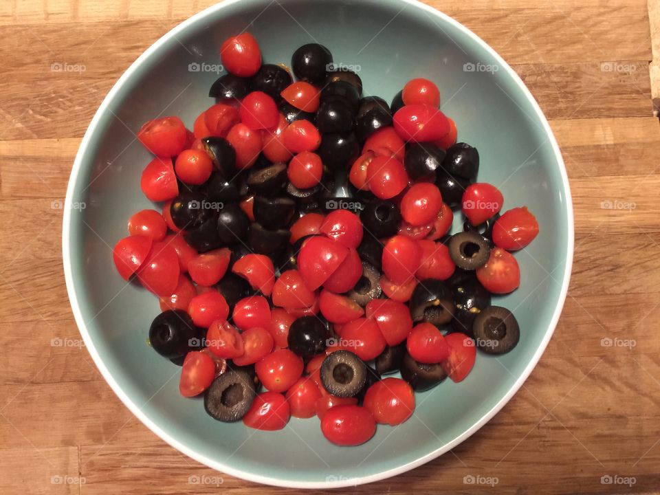 Cherry tomatoes and black olives cut up in a blue bowl 
