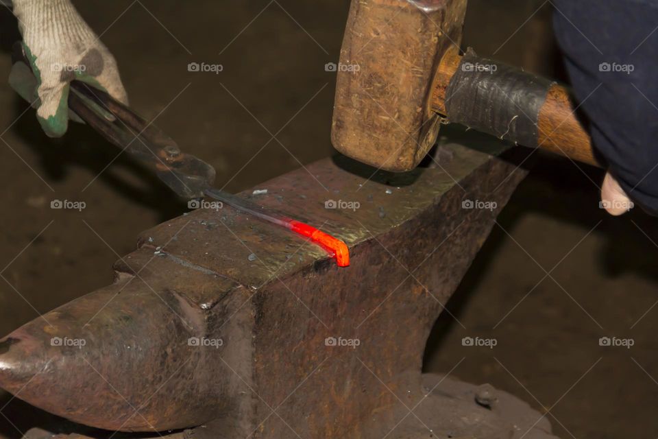 A blacksmith on an anvil makes a horseshoe and metal products from red-hot material.  Blacksmith workshop