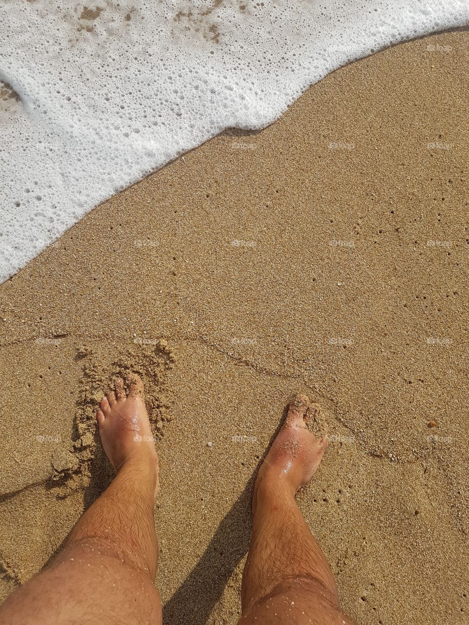 Legs in the water. Photopgraphed from above. Sand and salt water. Nice sunny day.