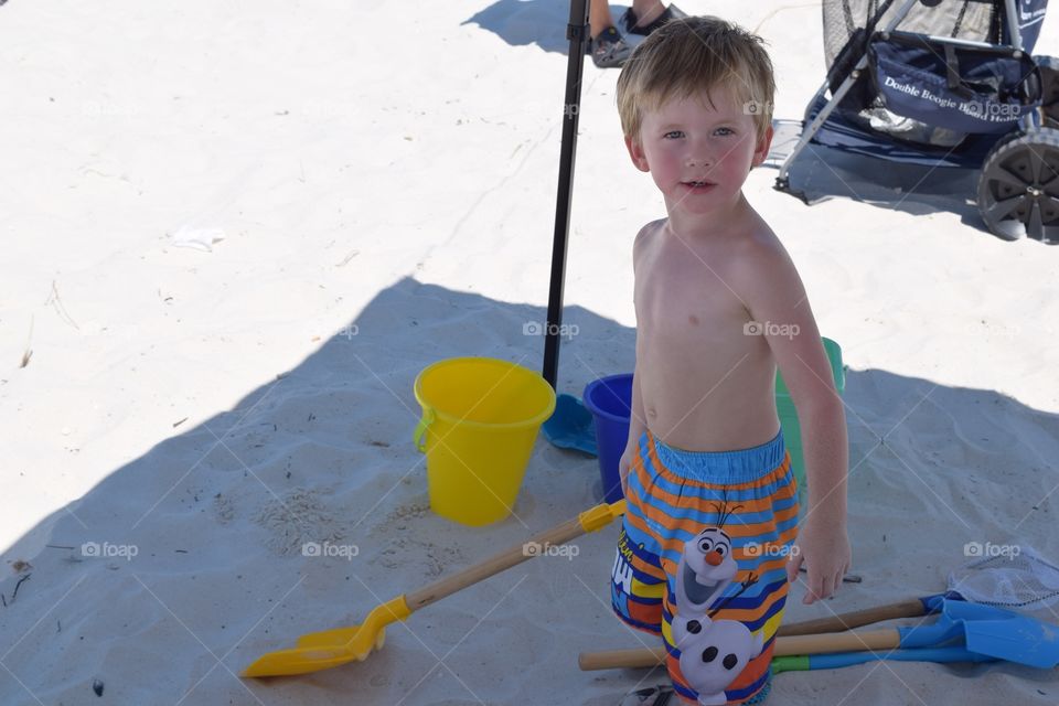Boy digging in the sand. Toddler enjoying the beach