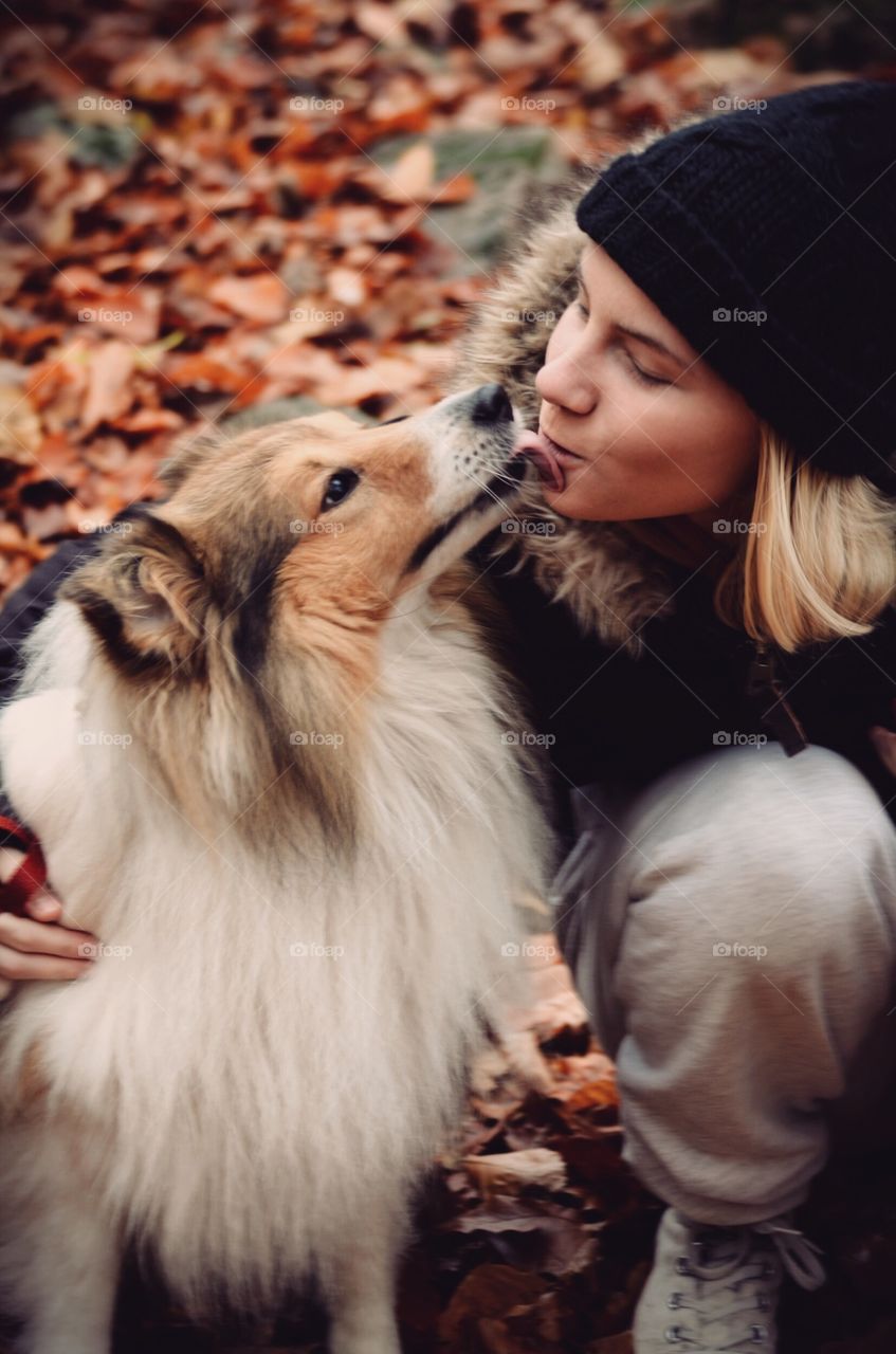 Portrait of a young woman or girl getting a kiss of a Sheltie Shetland Sheepdog dog outdoors in autumn