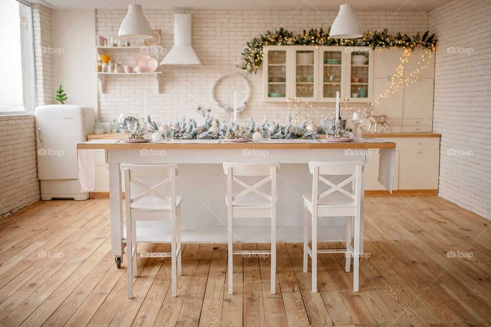 Festive winter cozy kitchen interior with garlands, decorations and gifts.  Christmas dinner at the decorated table.