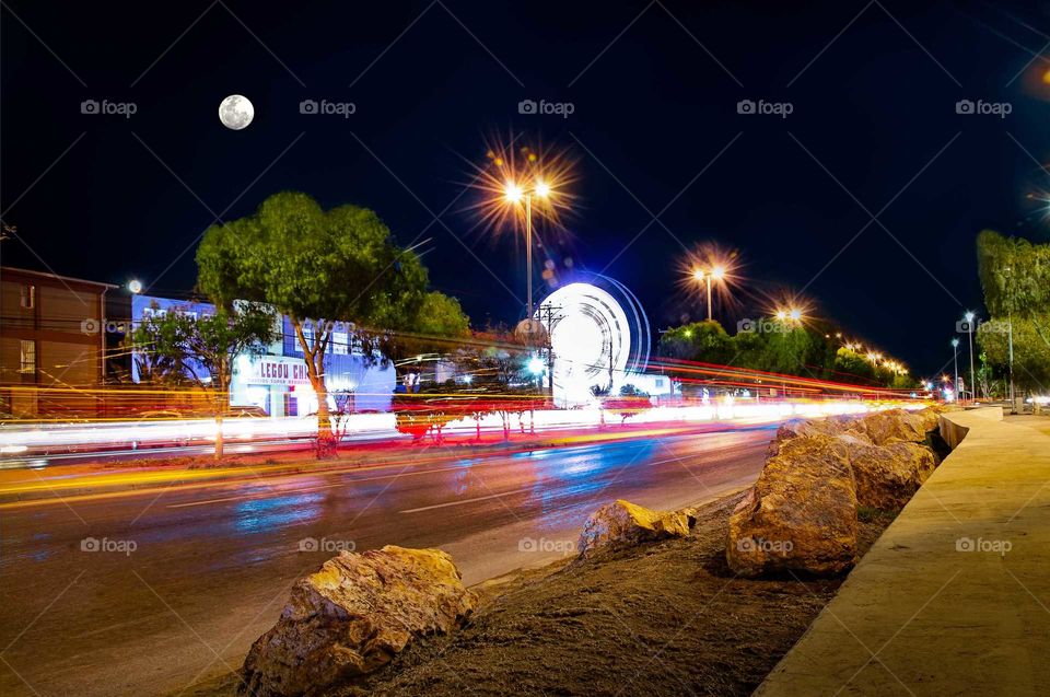 street illuminated by the flashes of passing cars and an entertainment park, in long exposure