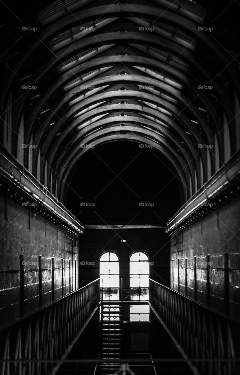 black and white photo of the inside of Melbourne Gaol (jail) with light coming through at end of gantry.