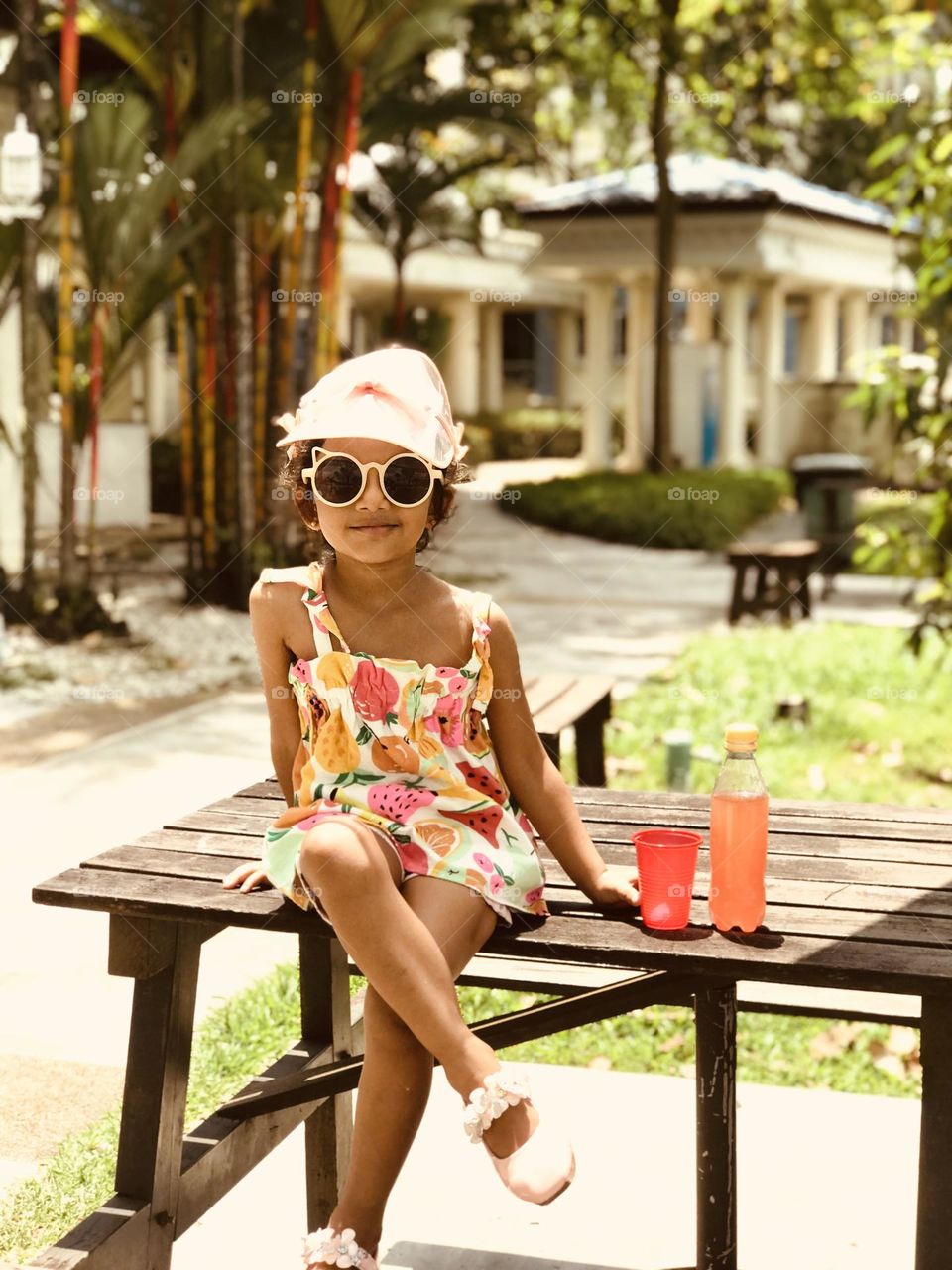 Cute Little girl in a summer outfits and sat on outdoor table with cool drink.
