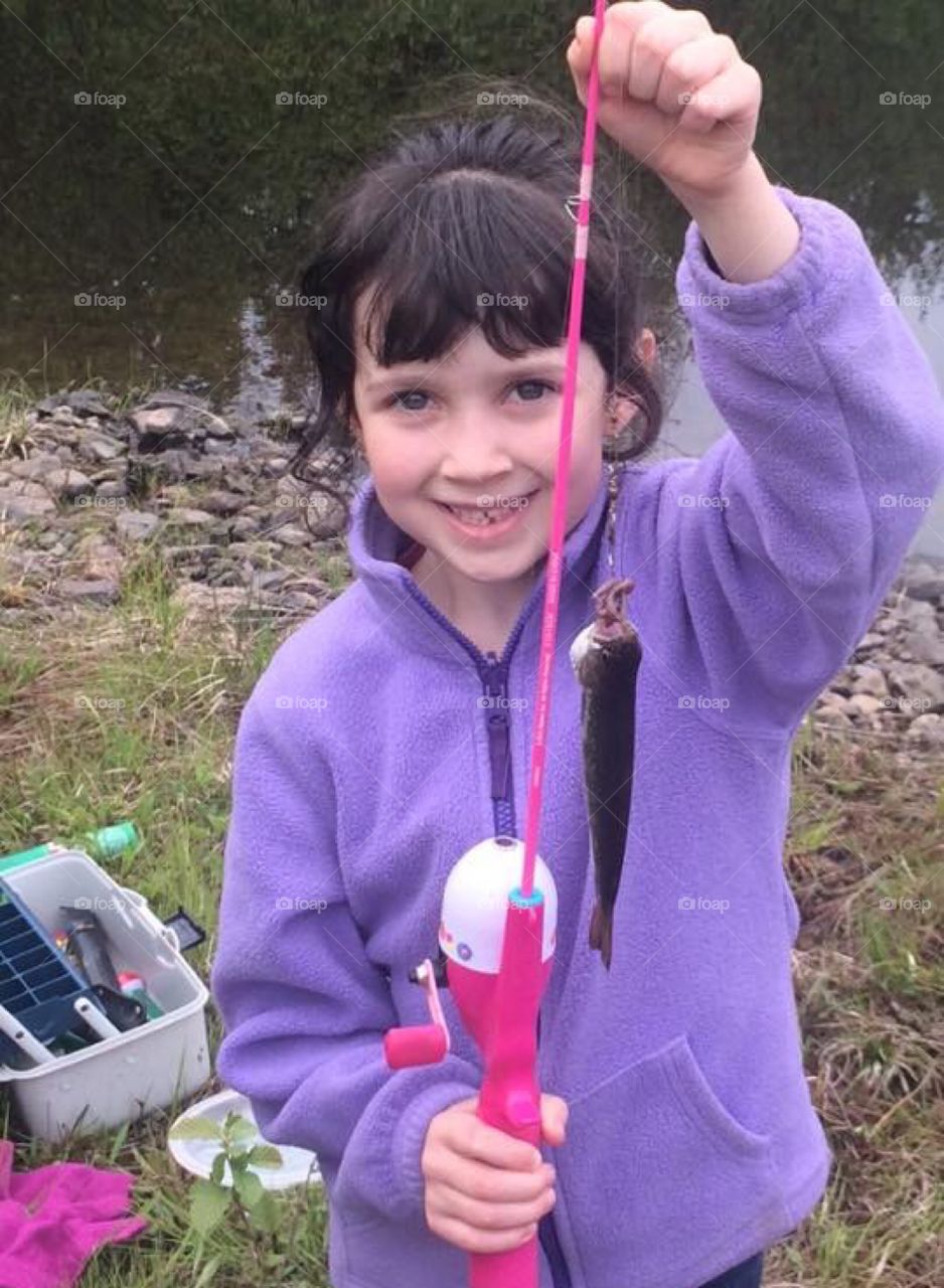 Proud little girl caught a fish with her pink fishing rod at the brook. 