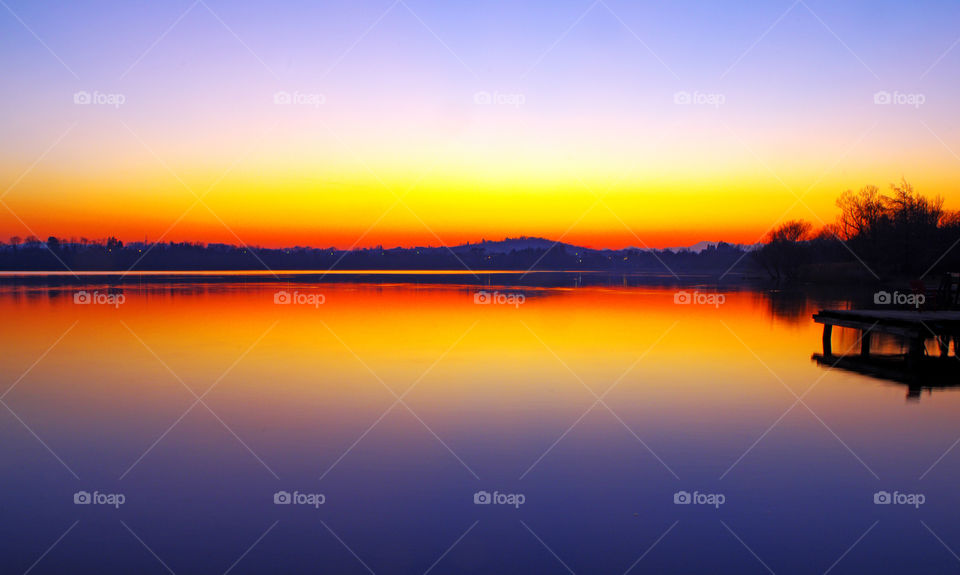 Sunset on Lake Varese with the hill which is reflected like in a mirror in the shaded waters by the colors of sunset.