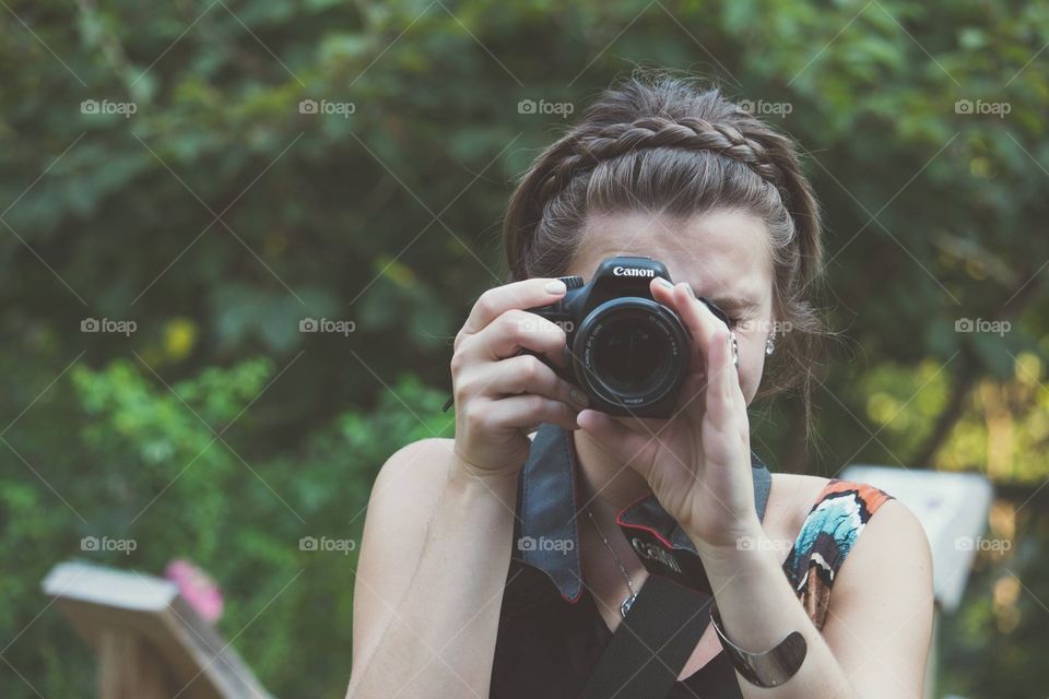 Girl or woman photographer holding Canon camera with braid outdoors taking photo