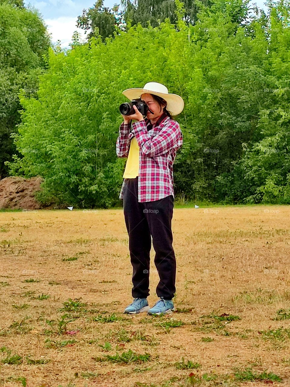 A girl stands on the field and uses a camera to shoot a cricket training session