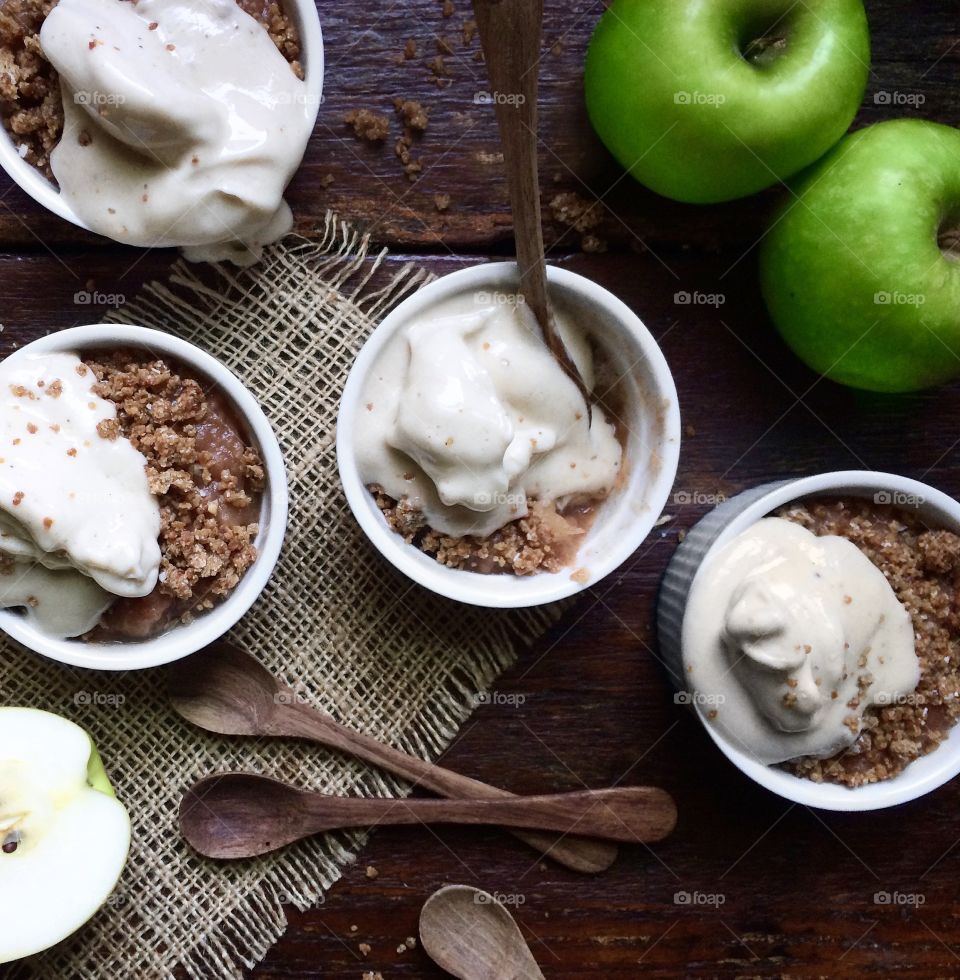 Apple crumble with melting ice cream in white bowls on wood table.