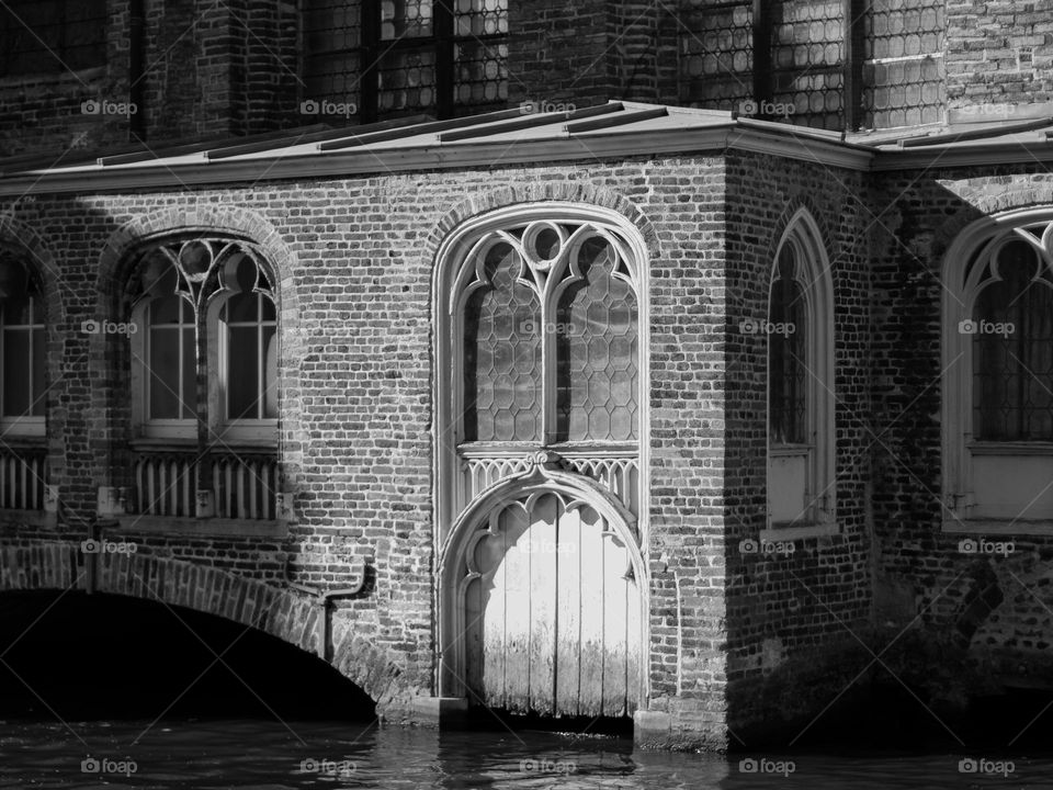 Beautiful view of an ancient residential brick house with geometric elements and patterns on the windows with wooden gates and an arch located on a canal in the city of Bruges in Belgium, close-up side view. Concept architecture of ancient houses and