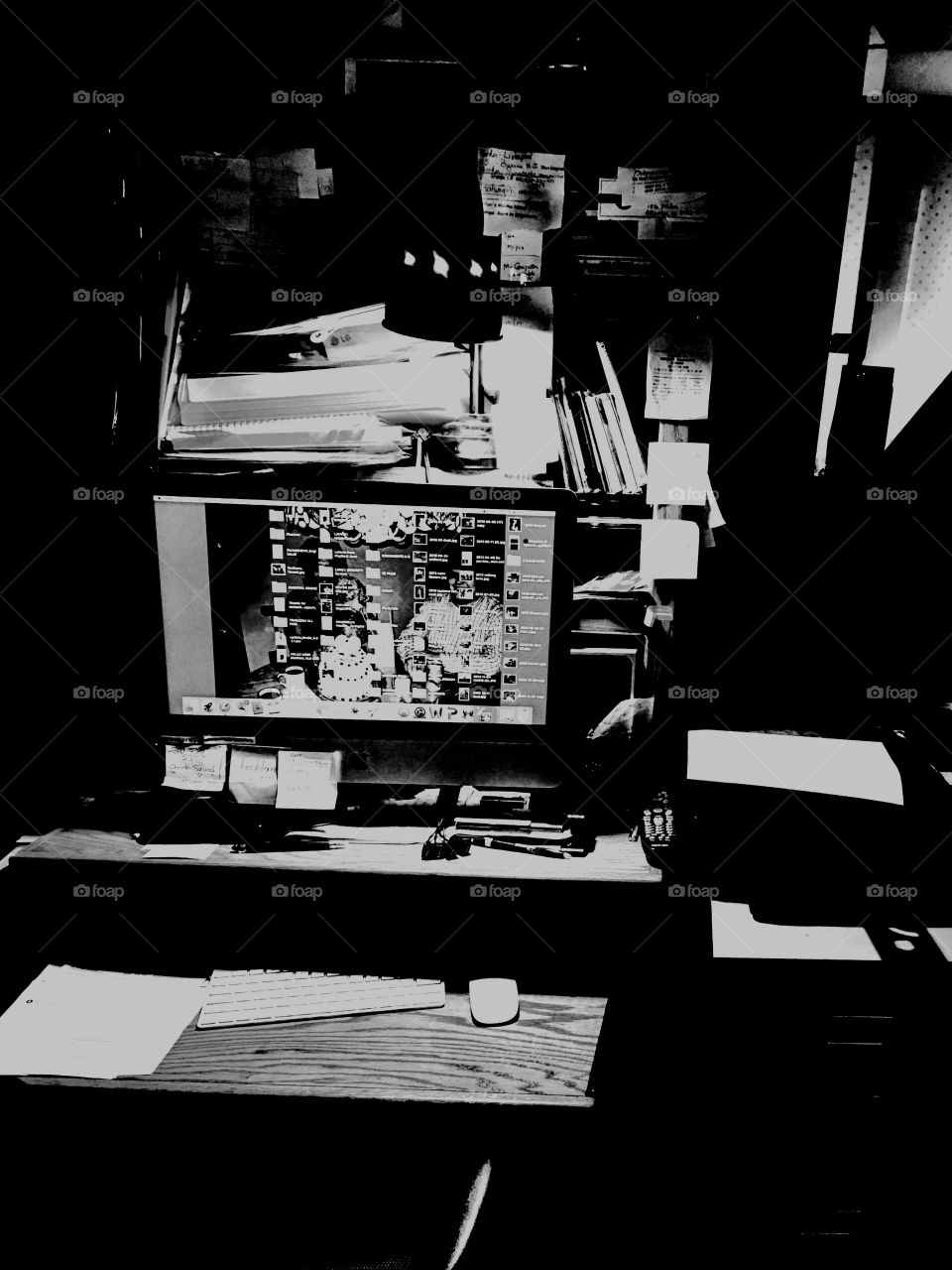 B&W photo of a home office computer desk. Work space is lit by a gooseneck lamp in the darkened room.