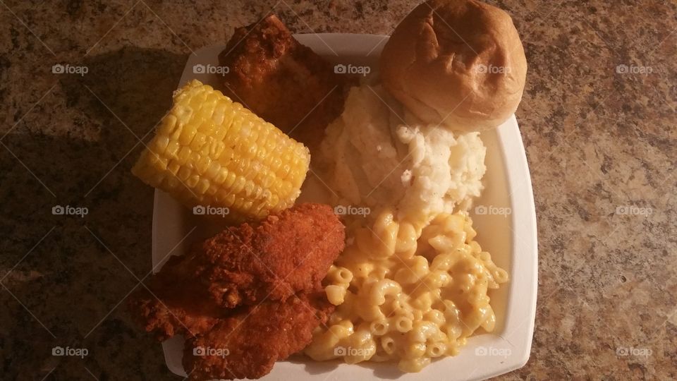 fried chicken, corn on the cob, fried pork chop, mashed potatoes, mac and cheese and a dinner roll