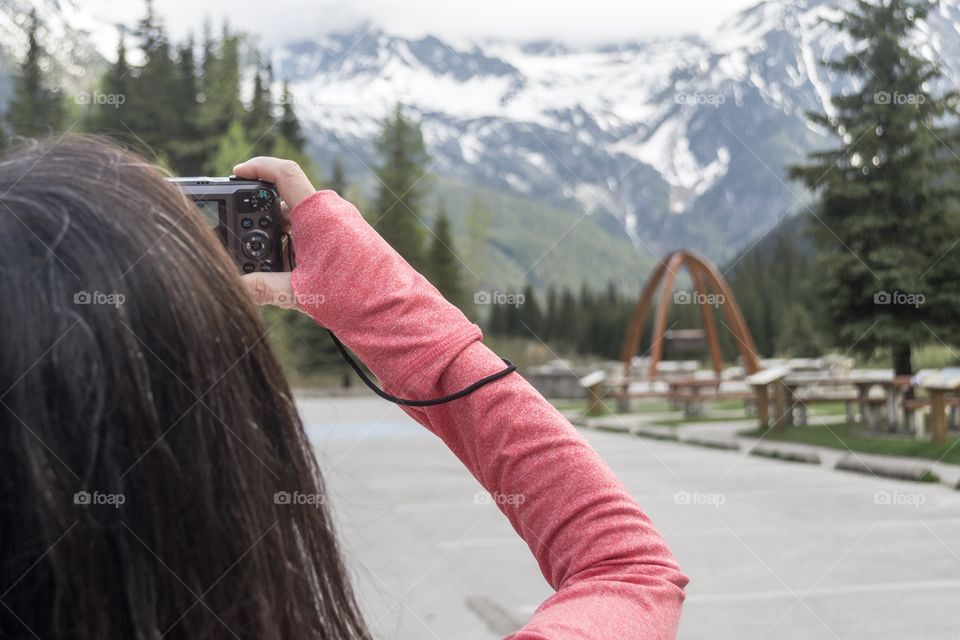 Female photographer in red long sleeve top capturing photo of snow capped Canadian Rocky Mountains using DSLR camera