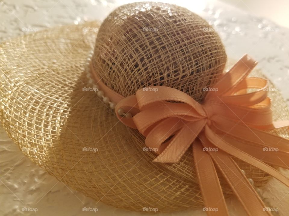 light glisten of the top of a lightly woven hat,  adorned with a pearl band and abundant peach ribbons