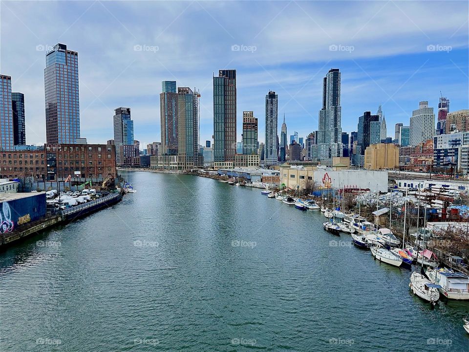 This is „Newtown Creek“ with its many boats seen from the „Pulaski Bridge“ that connects „Greenpoint“, Brooklyn to LIC, Queens. In the distance across the waters of the „East River“ we see „Manhattan“. 2024. Hypnotic Productions
