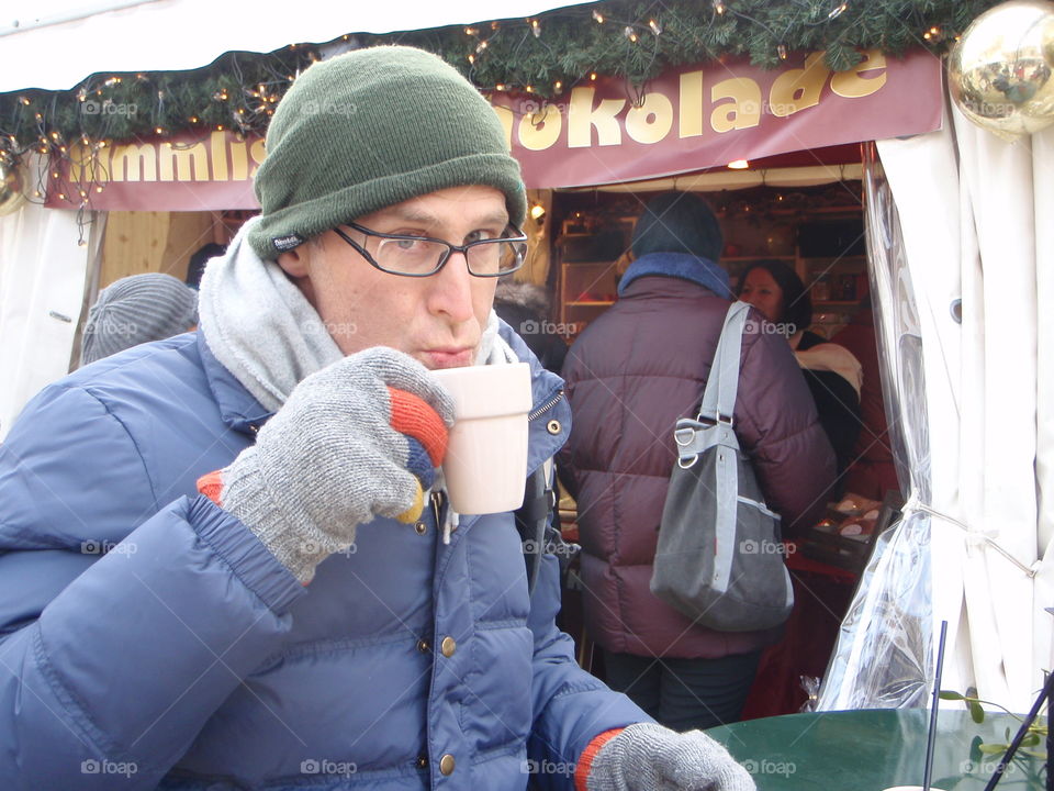 Hot chocolate at outdoor Christmas market europe. Rugged up in coat and hat. Cold. Man in blue coat enjoying hot chocolate.