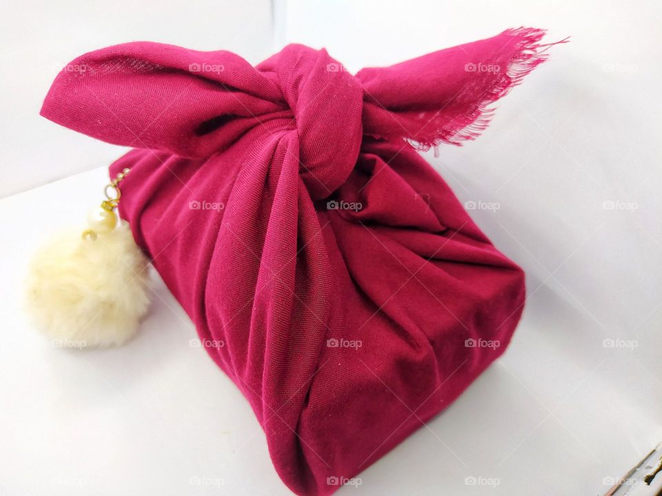 A gift wrapped in a red cloth. Adorned with a white fluffy ball hanger. Birthday gifts. Isolated on a white background.