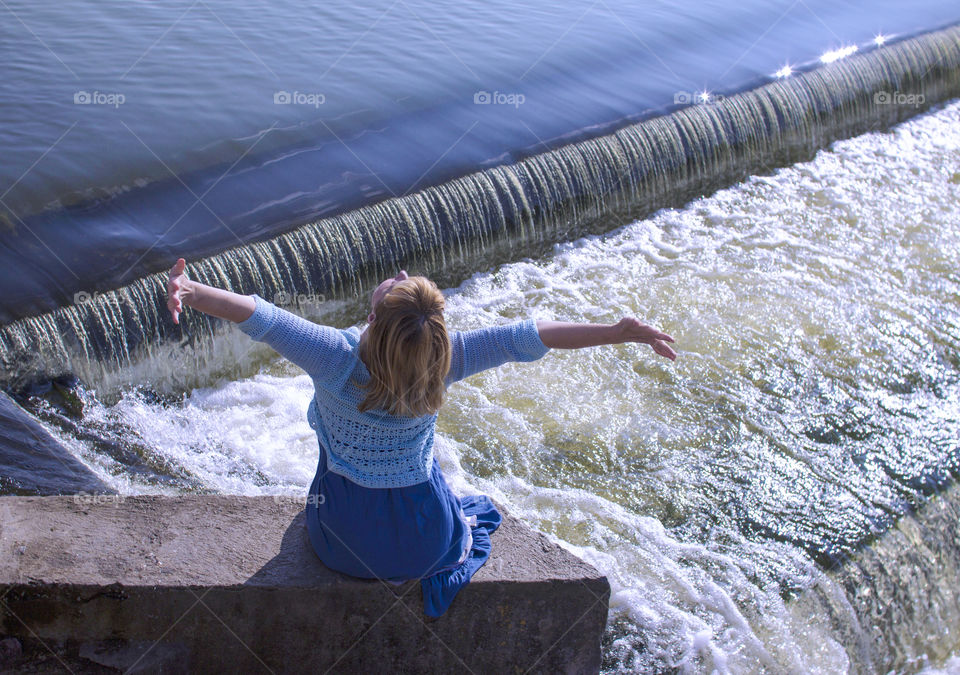 The girl is sitting on the bridge near the lake