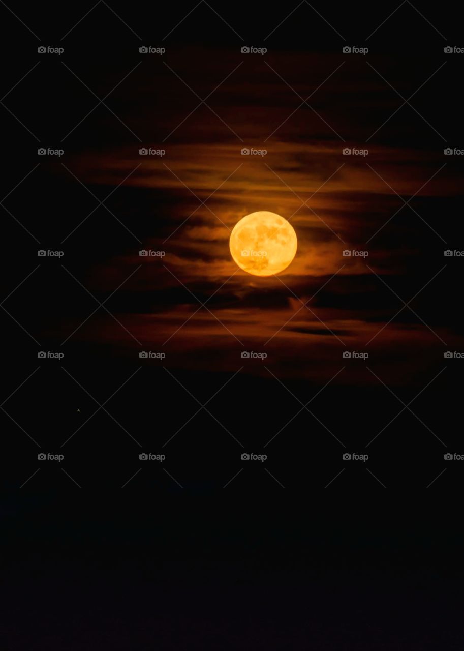 beautiful autumn full moon glowing a deep yellow orange color with clouds sweeping across it leaving deep yellow orange trails in the sky all around the moon