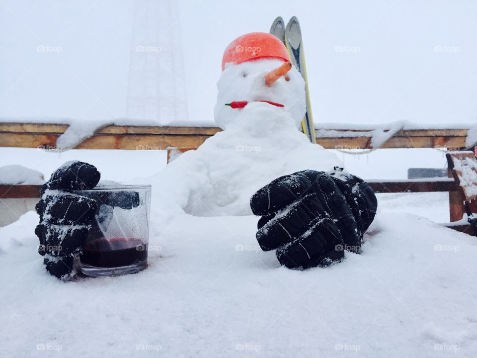 Funny snowman sitting at a table wearing gloves and holding a glass of drink