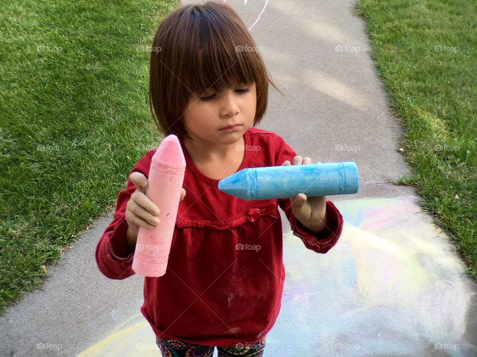 Little girl on walkway in park with crayons in hand