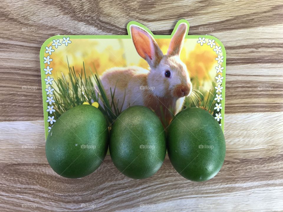 Easter bunny, Easter bunny card with three green eggs in front of the card ona a wooden table.