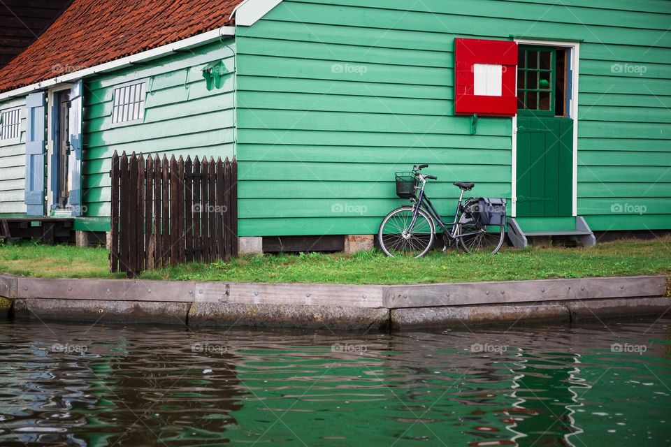 A lone bicycle standing by the green wall of a house near the water, displaying a quiet and tranquil rustic scene