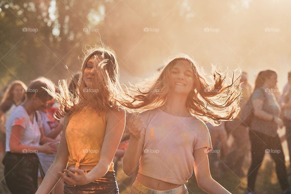 Portrait of happy smiling young girls with colorful paints on faces and clothes. Two friends spending time on holi color festival