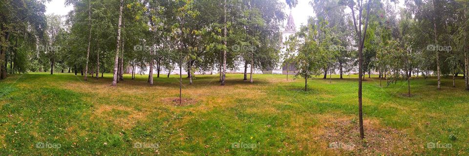 Panorama.  An ancient white fortification in the form of a wall and an observation tower, around which there are green trees