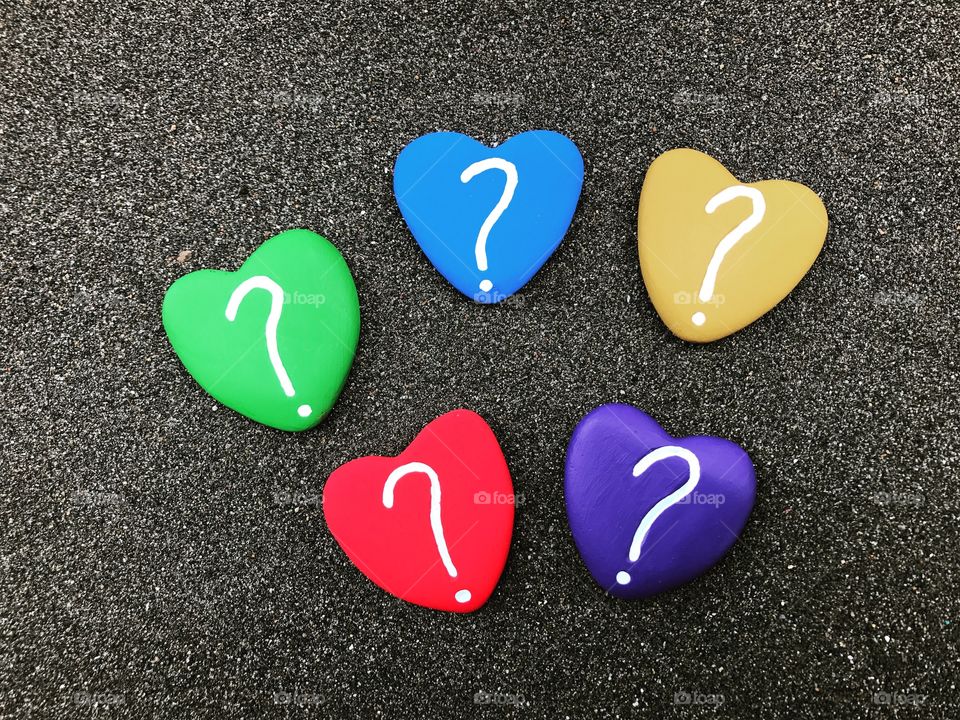 Question marks with colored heart stones over black volcanic sand