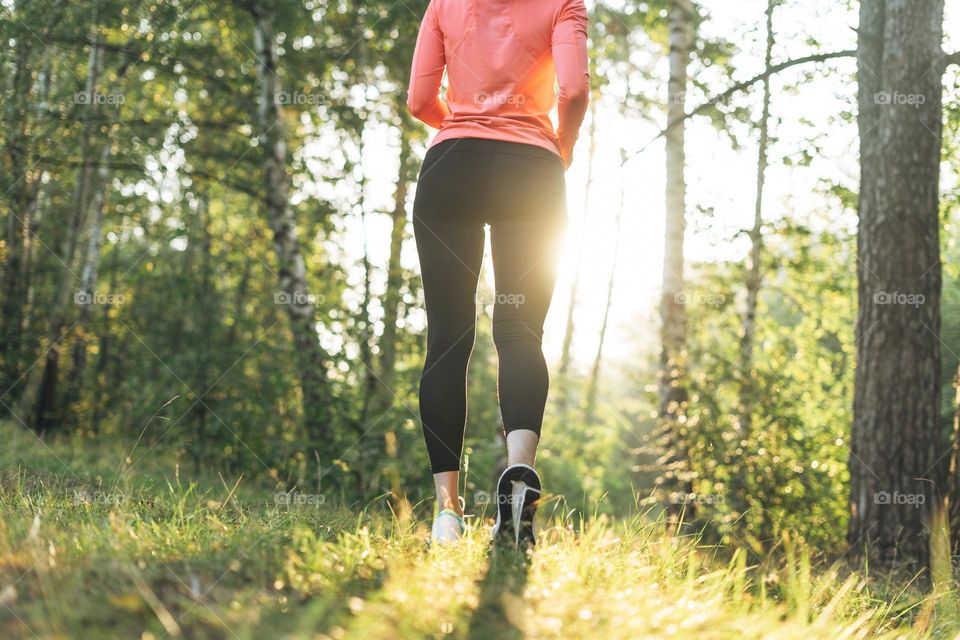 Young slim woman brunette in sport clothes running at autumn park on golden hour sunrise time. Health and wellness, fitness lifestyle