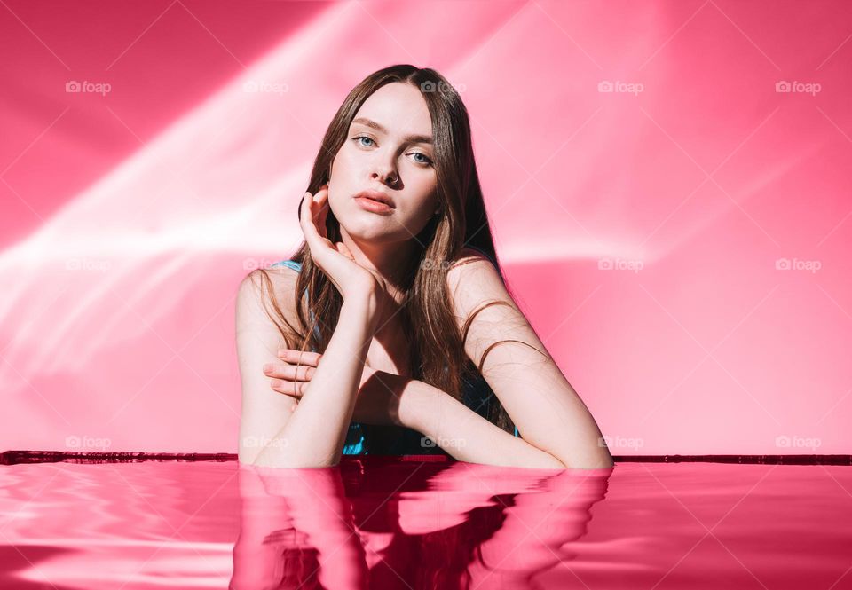 Beauty portrait with water of young woman fashion model with healthy dark long hair on viva magenta colour background