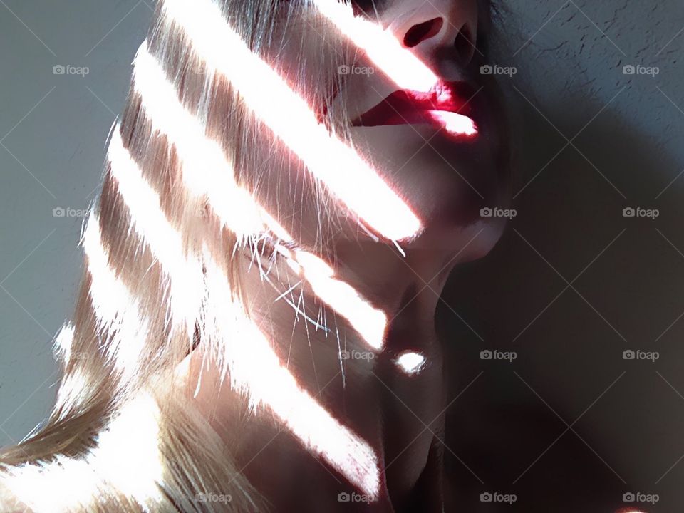 Diagonal lines of bright sunshine contrast with shadows along a woman’s face.
