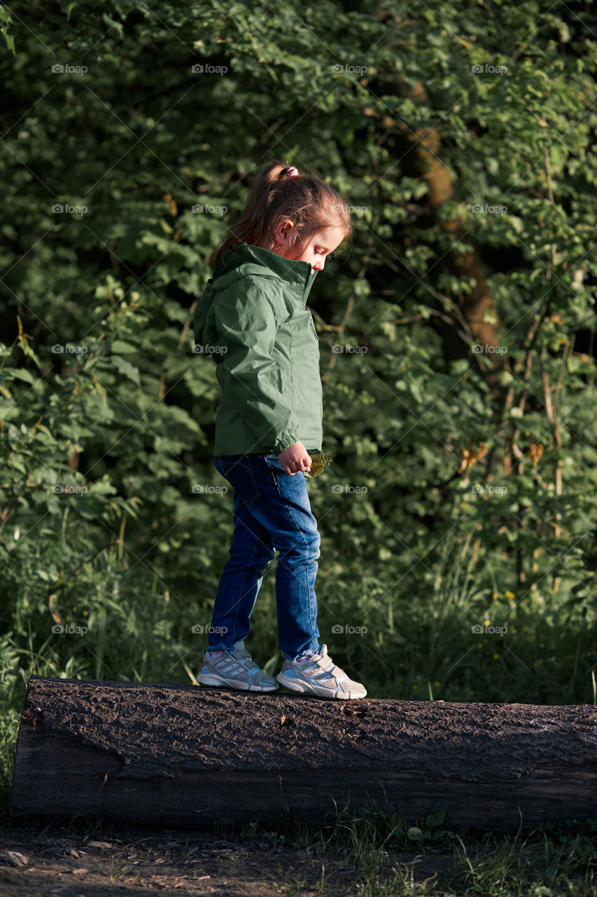 Little girl walking on stump in forest, playing during walk